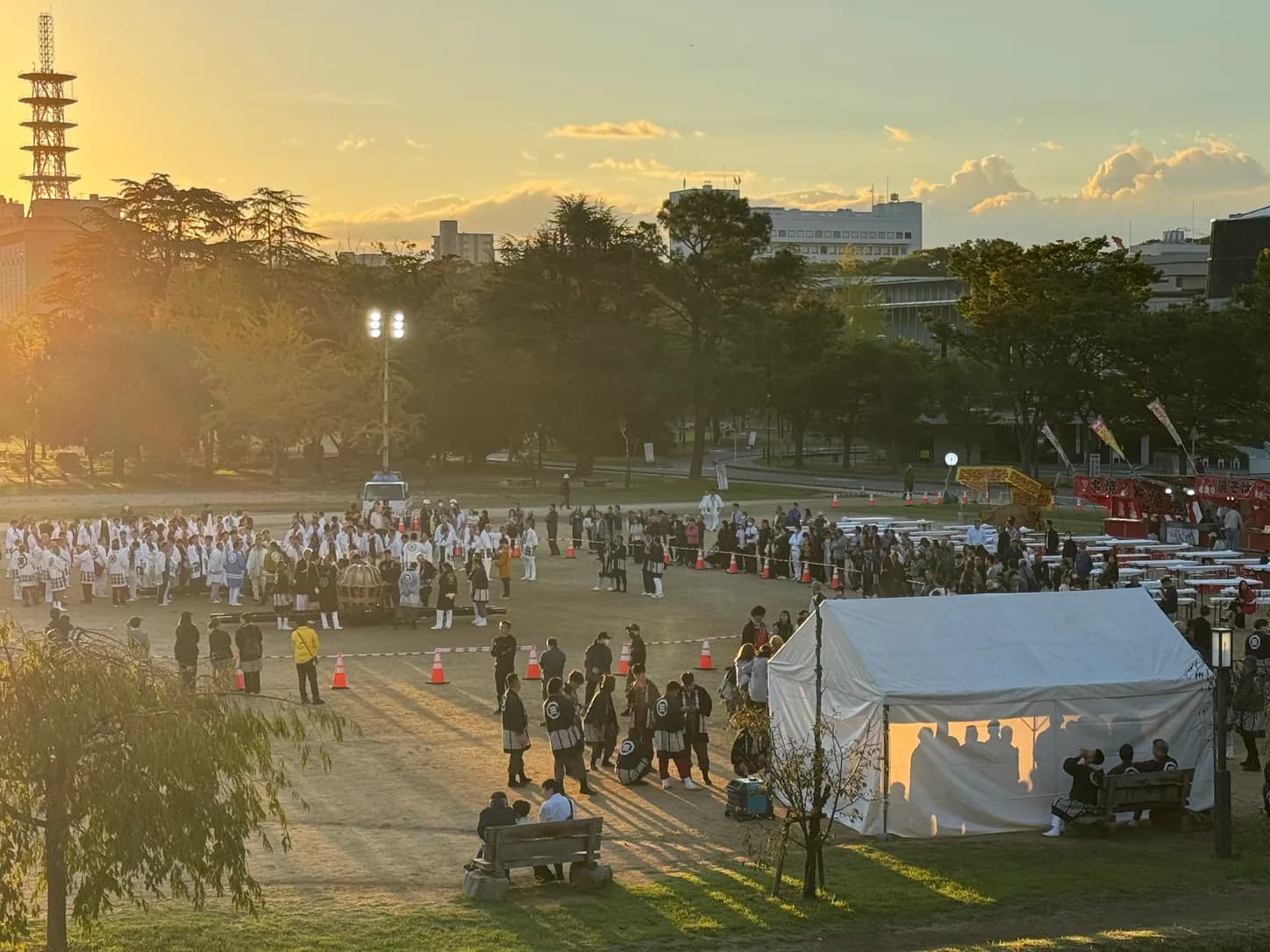 夜明けの城山公園。ロープで囲われた広場に担ぎ手が整列し、周りを見物の人が囲みます。土手の上から。