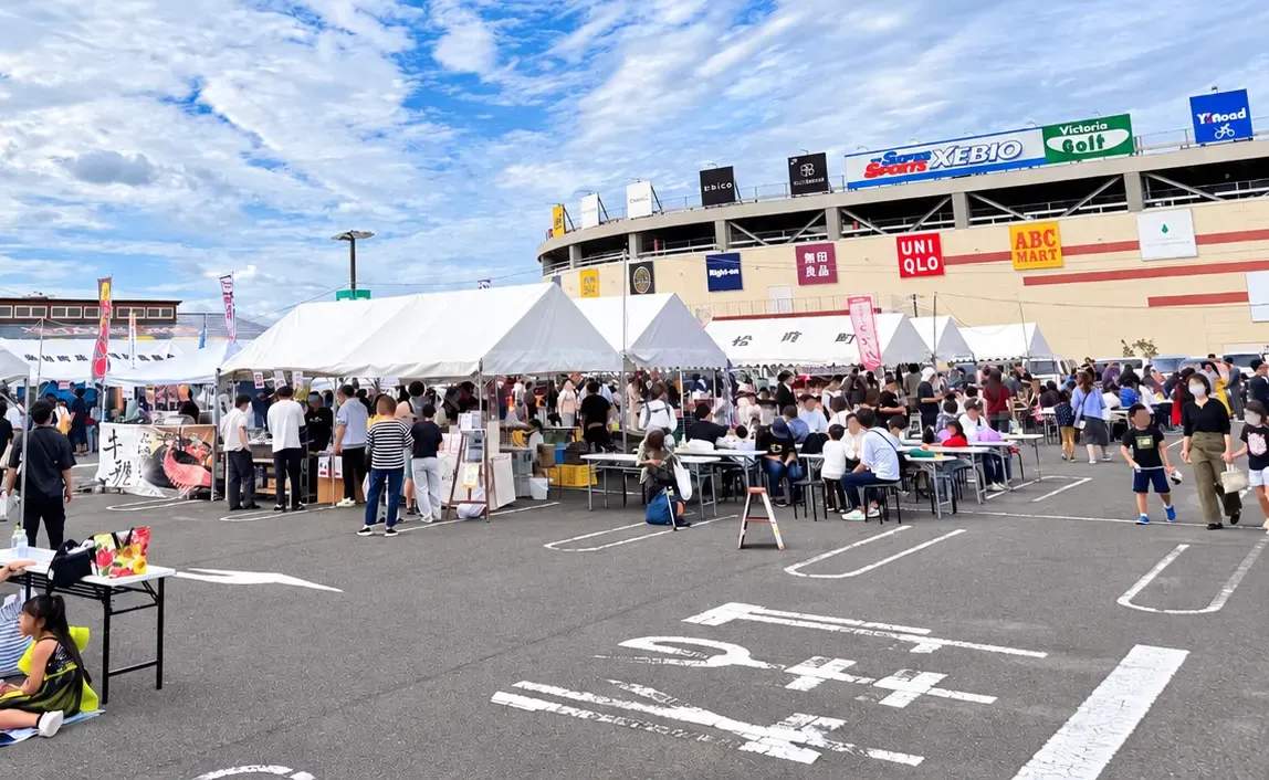 エミフルMASAKIを背に、まさき村前の駐車場に白いテントが並び、テーブル席で食事をする人でにぎわう会場